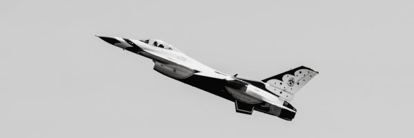 Monochrome image of a military aircraft soaring against a grey sky.