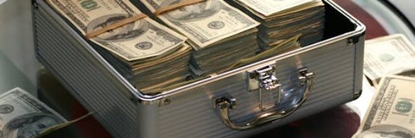 Open briefcase filled with stacks of hundred dollar bills on a glass table, representing wealth.
